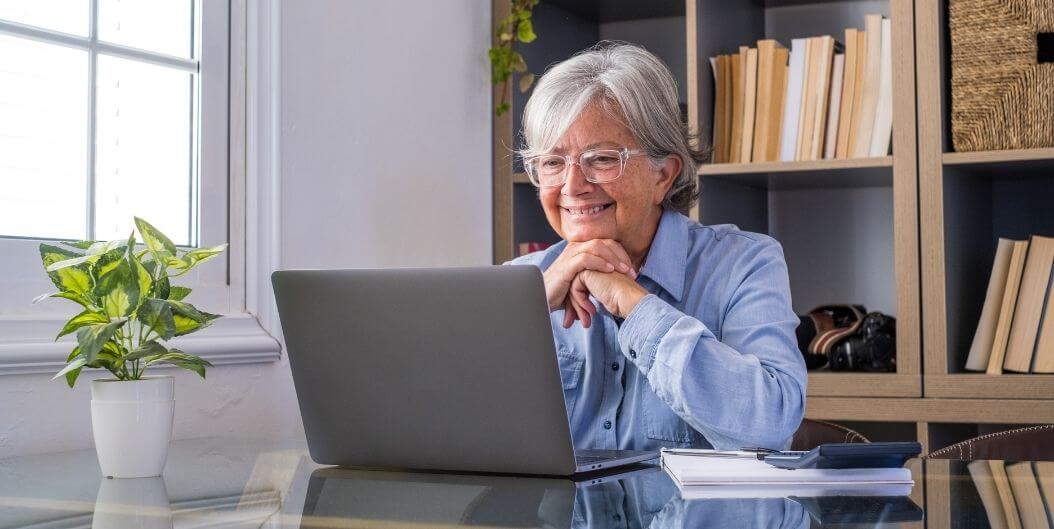 Elderly Woman Typing On Laptop In Bright Room At Independent Living Facility