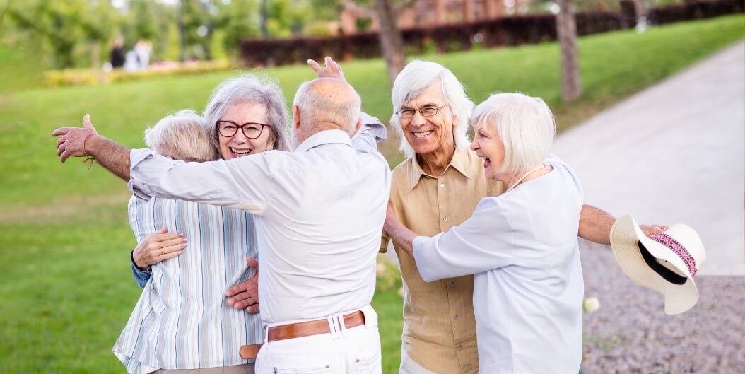 Group of Seniors Embracing and Greeting Each Other Outdoors at an Independent Living Facility